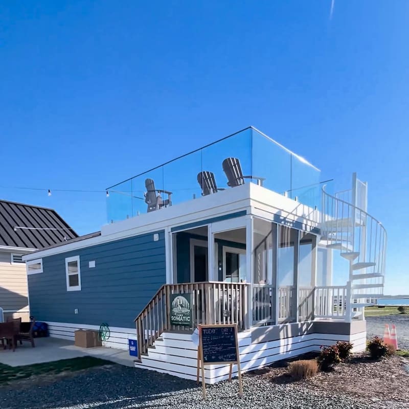 A blue tiny cabin with a glass rooftop deck and a spiral stair, from the Camp Somatic ad.