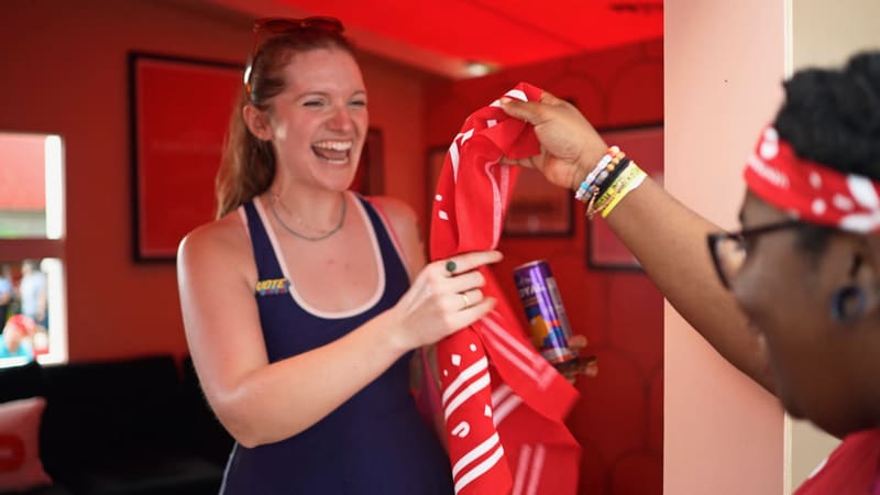 A festival guest laughing as staff hand her a bandana inside a red-lit room at DoorDash’s activation.