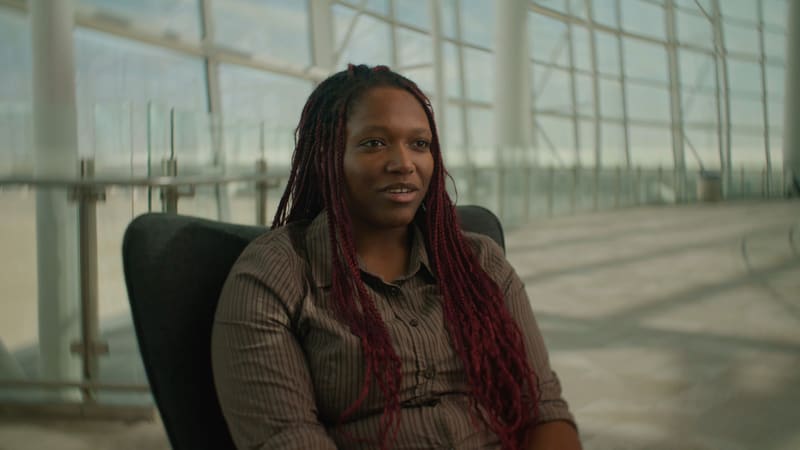 A young woman with long burgundy braids interviewed in a sunlit glass atrium, from Education Strategy Group’s Indianapolis spotlight.