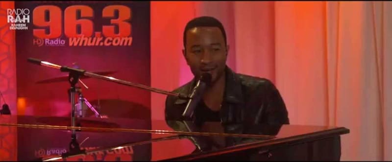 John Legend at a piano in the Studio202 studio, with a 96.3 WHUR banner behind him.